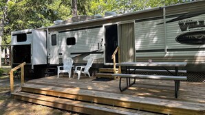 A mobile home with a deck, two chairs, and a picnic table. - Twin Birch Resort - The Loon on the Lake - Lakefront with Dock, Kayak, and Rowboat! (Honor)