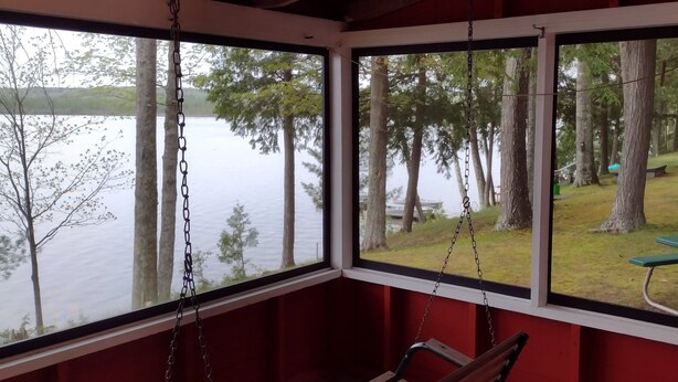 Une cabane avec un fauteuil suspendu et une vue sur un lac et une forêt.