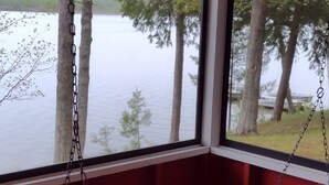 Une chaise suspendue en bois, fixée à une chaîne et à une structure rouge et blanche, offrant une vue sur un lac et des arbres.
