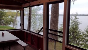 Un espace extérieur abrité, avec une table et des bancs, offrant une vue sur un lac bordé d’arbres et sur une rive éloignée.