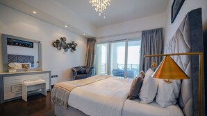 Une chambre moderne avec un grand lit, un bureau et une chaise. Elle dispose d’un balcon avec vue sur l’extérieur.