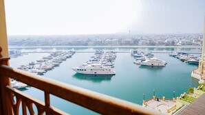 Un port de plaisance où sont amarrés de nombreux yachts, une vue dégagée sur le paysage urbain en arrière-plan et une balustrade de balcon au premier plan.