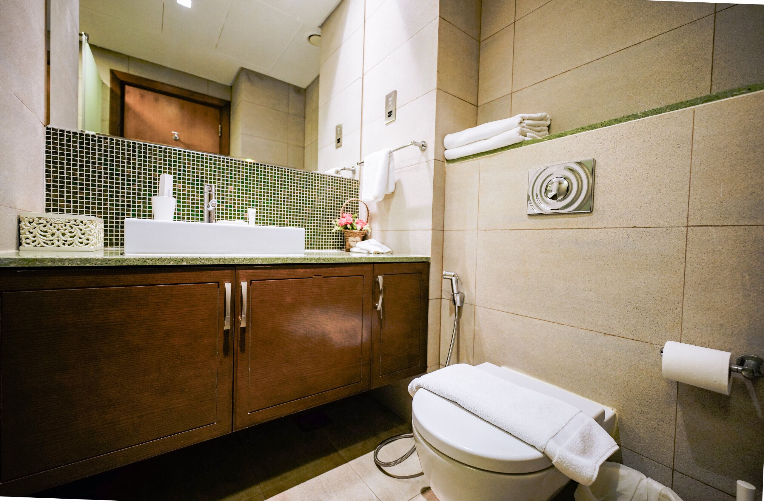 A bathroom with a wooden vanity, a white sink, a toilet, and a green-tiled shower area.