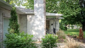 A brick house with a porch, surrounded by greenery and a well-maintained lawn. - Charming Rancher, Close to Everything! (Joplin)