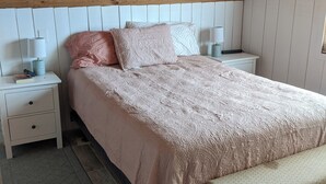 Un dormitorio con techo de madera, una cama con colcha estampada, dos mesitas de noche con lámparas y un banco al pie de la cama.