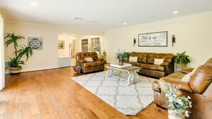 A spacious living room with two brown leather sofas, a white rug, and a coffee table. There are potted plants and wall art. - Game Room! Group Getaway 16 Mi to Galveston (Hitchcock)