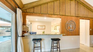 A kitchen area with wooden paneling, a bar counter with stools, and a view of the outside. - Game Room! Group Getaway 16 Mi to Galveston (Hitchcock)