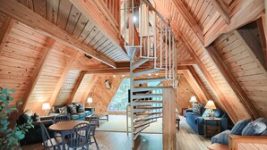 A spacious loft with a wooden interior, a spiral staircase, and a large window offering a view of the outdoors.