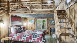 A rustic room with a bed, a wooden ladder, and a window with a view of trees.