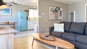 Un salon moderne avec un canapé gris, une table basse en bois et une cuisine en arrière-plan.