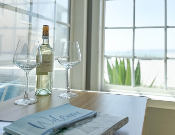 A table with a bottle of Pinot Grigio and two empty wine glasses, a notebook with "Welkommen" written on it, and a view of the sea through a window. - Sea View Escape (San Clemente)