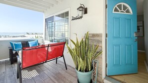 A covered outdoor seating area with a red bench, a potted plant, and a blue door.