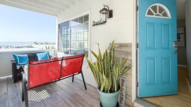 Un espace extérieur abrité avec des sièges, comprenant un banc rouge, une plante en pot et une porte bleue.