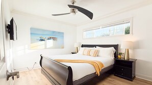 A bedroom with a bed, a nightstand, a lamp, a painting, and a ceiling fan. - Golden Coast Ocean View Penthouse (San Clemente)
