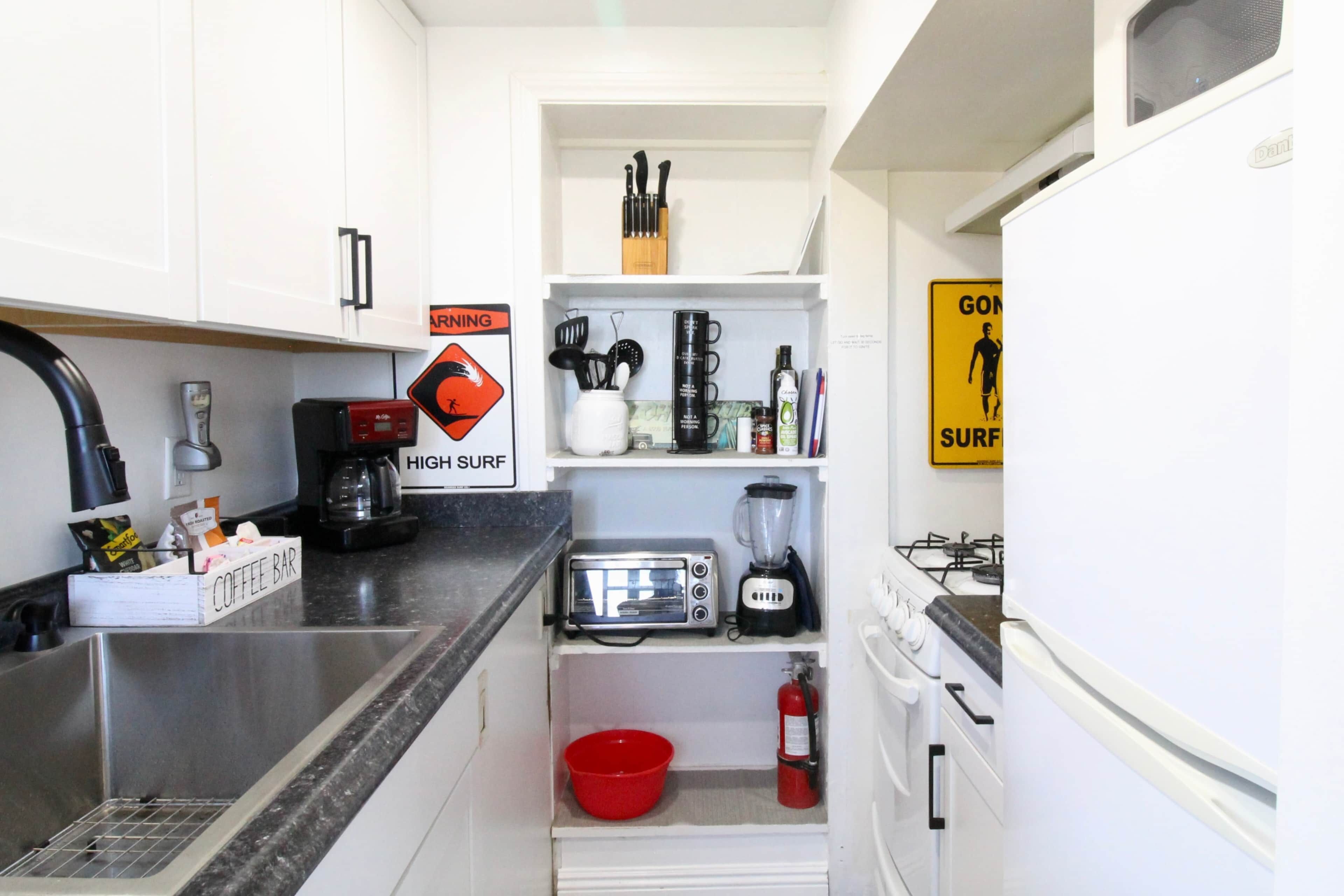 A compact kitchen with white cabinets, a coffee bar, a toaster, a blender, and a fire extinguisher.