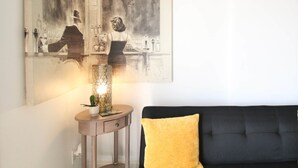 A living room with a black sofa, a yellow pillow, a small round table with a lamp, and a large abstract painting on the wall. - Ocean Bluff Hideaway (San Clemente)
