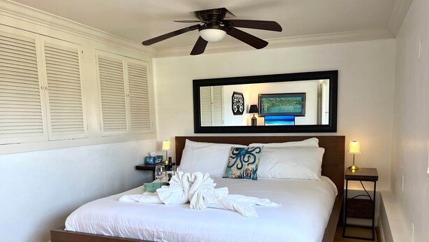 A neatly made bed with white linens, a wooden headboard, and a ceiling fan. - Ocean Bluff Hideaway (San Clemente)