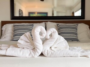 A bed with white linens and striped pillows, and a mirror reflecting a painting. - Ocean Bluff Hideaway (San Clemente)