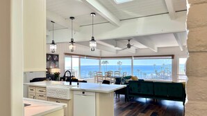 Une cuisine moderne dotée d’un îlot central, de luminaires suspendus et offrant une vue sur l’océan.