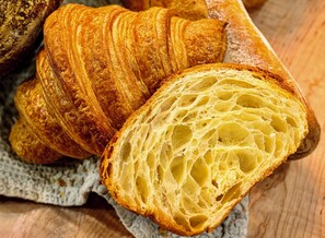 A close-up of a croissant with a flaky, layered texture and a golden-brown crust. - Meeting House Boutique Hotel (Falls Church)