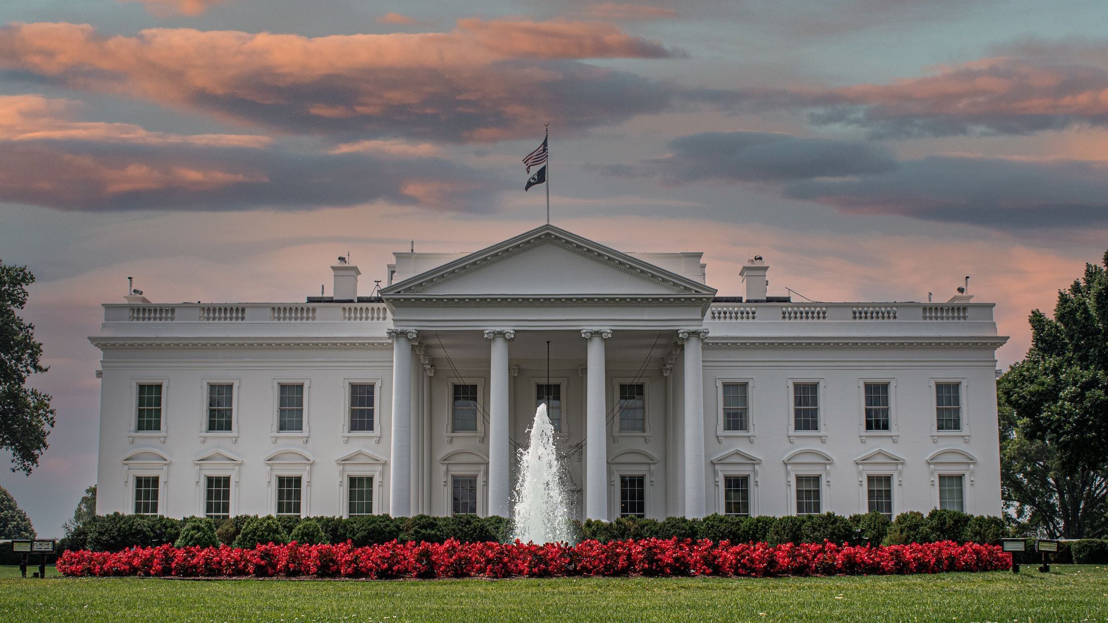 A large white building with columns, a flag, and a fountain in front.