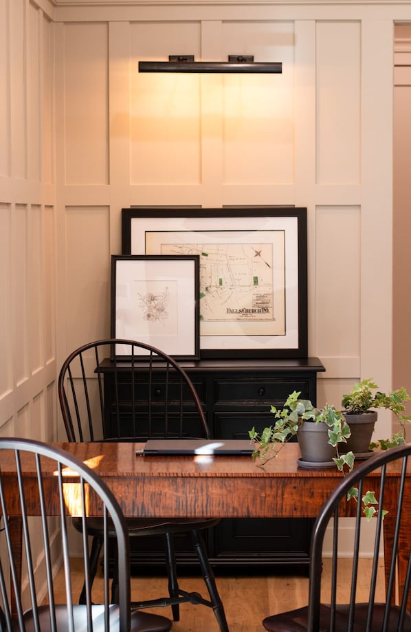 A dining area with a wooden table, black chairs, a laptop, and framed maps on a black cabinet. - Meeting House Boutique Hotel (Falls Church)