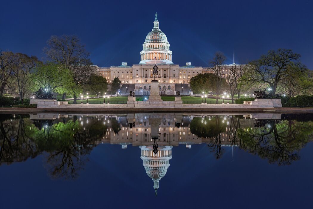 A large, illuminated building with a dome, surrounded by trees and a reflective water body.