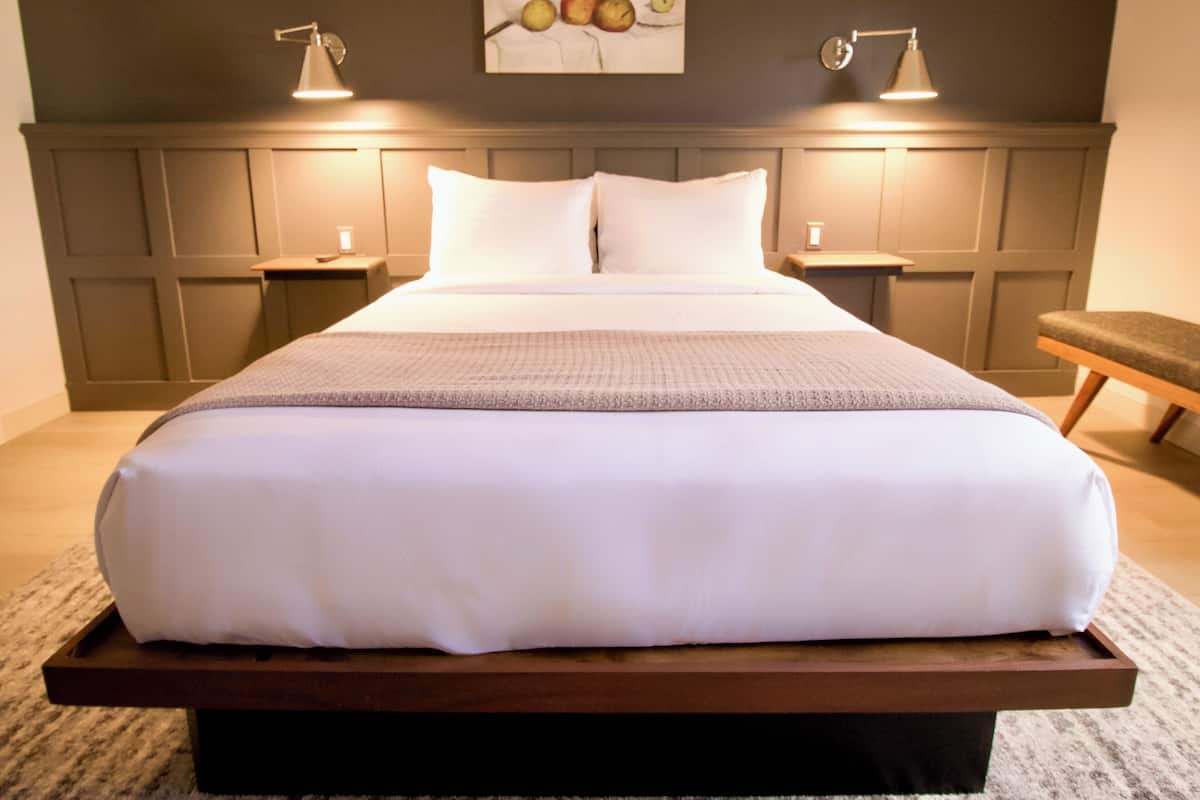 A large bed with a wooden platform, two bedside tables, and a wall-mounted lamp.