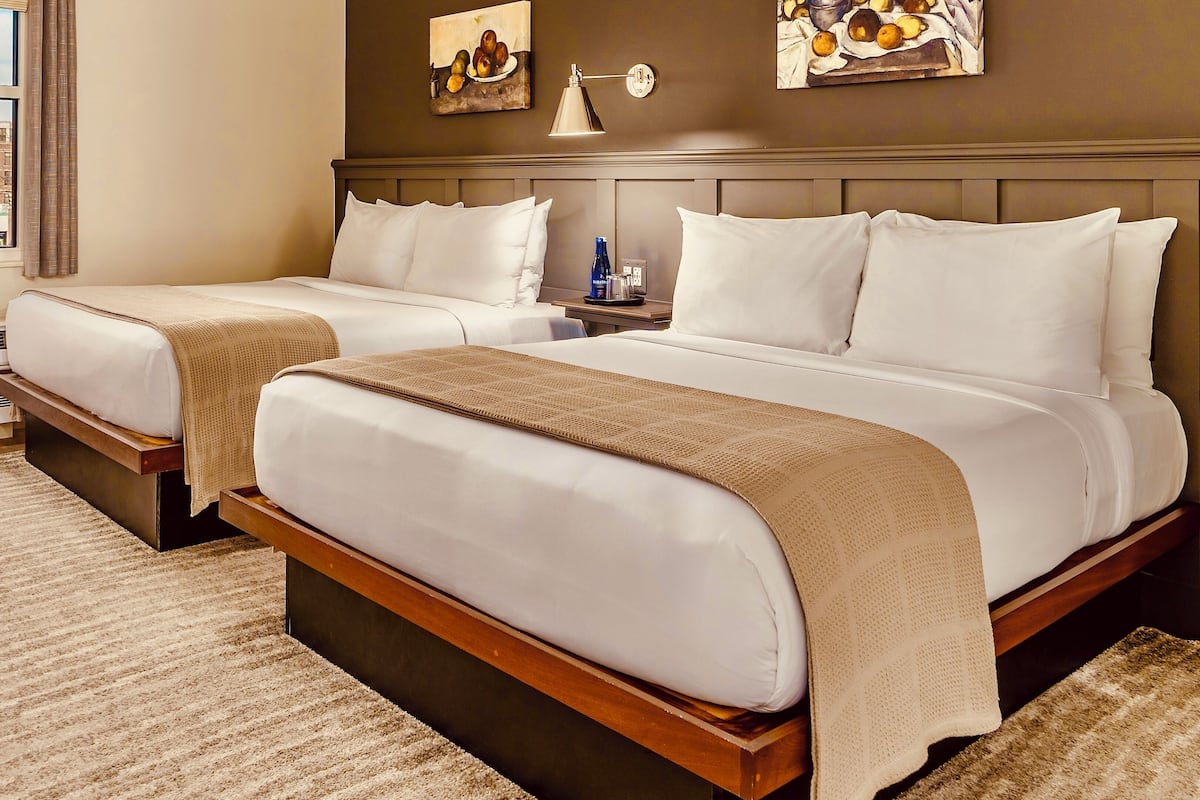 A hotel room with two beds, a nightstand, a lamp, and artwork on the walls.