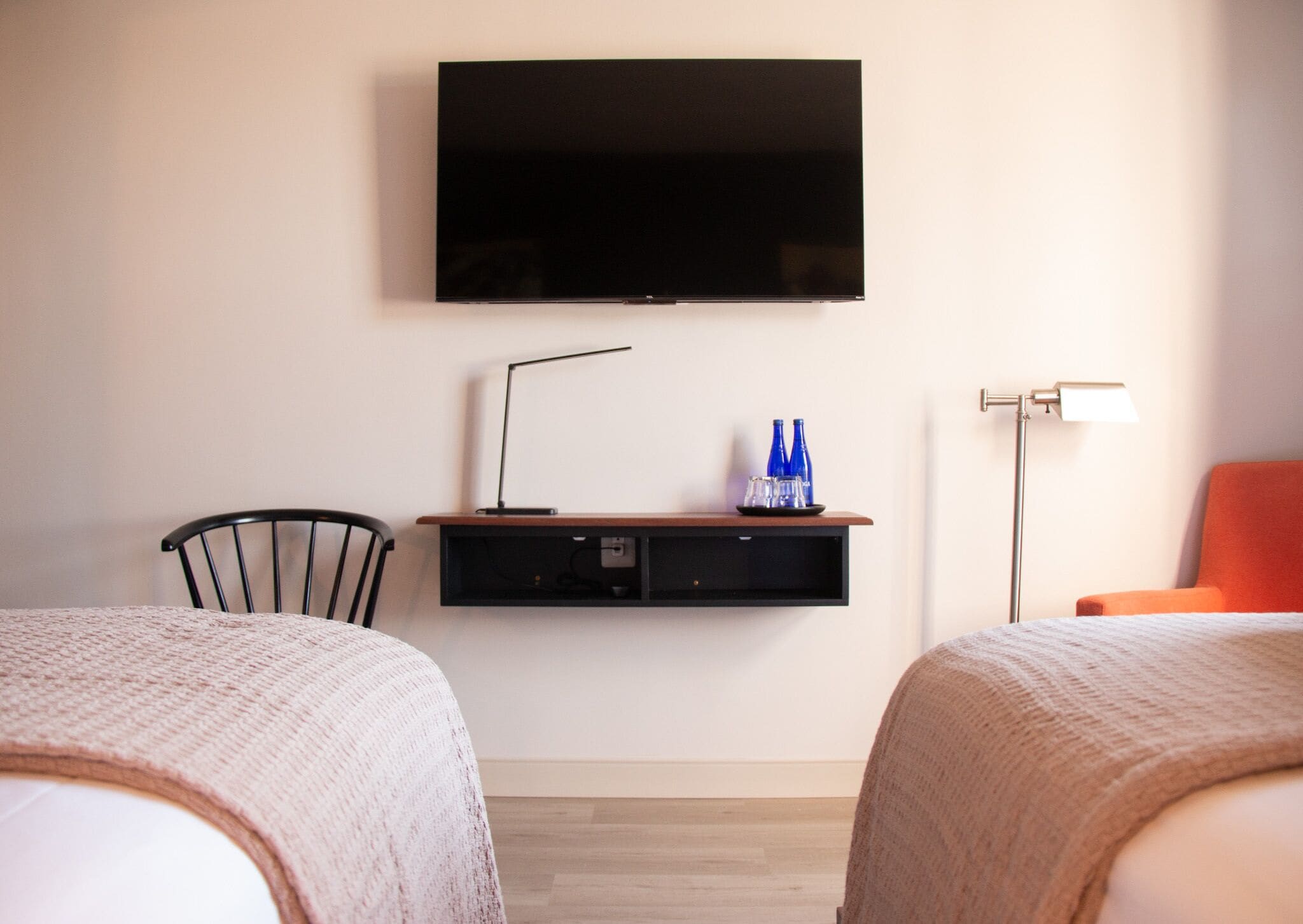 A hotel room with two beds, a TV mounted on the wall, a desk with a lamp, and a chair.