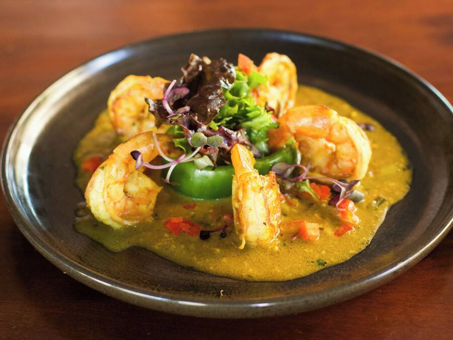 Une assiette de nourriture contenant des crevettes et des légumes, le tout présenté sur une assiette foncée.