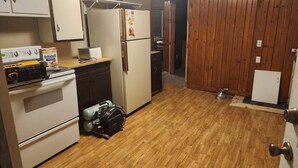 Una cocina compacta con estufa, refrigerador y lavavajillas. El suelo y la pared son de madera.