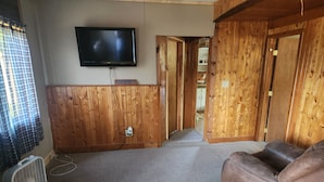 Una habitación con una televisión montada en la pared, un sofá de cuero marrón y suelo de madera.
