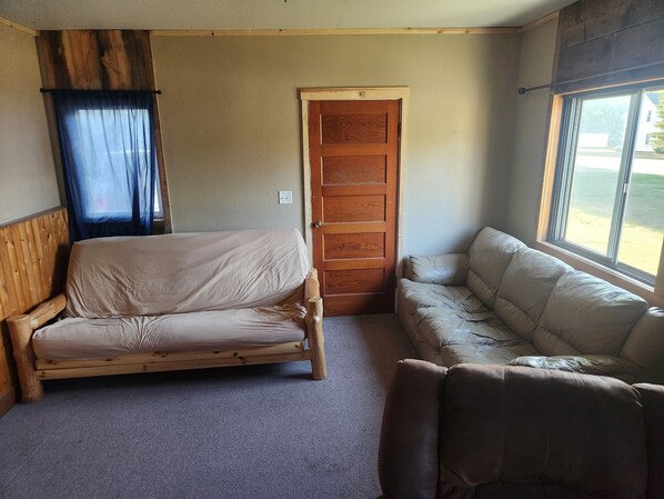 A compact room with a wooden bed, a cushioned bench, a door, and a window with a view. - HUNTERS!! Are you looking for a house while you are in North Dakota? Here it is! (Tolna)