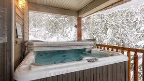 Un bain à remous sur une terrasse en bois, avec vue sur des arbres couverts de neige.