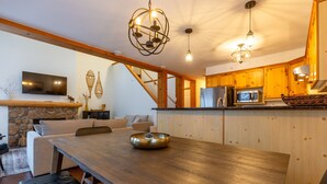 Une cuisine moderne avec des meubles en bois, un mur en pierre, un téléviseur à écran plat et un coin repas comprenant une table et un banc en bois.