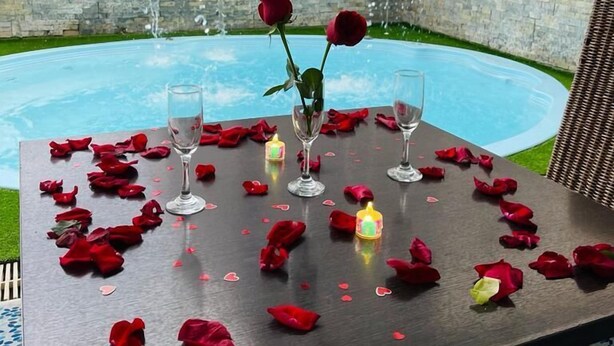 Ein Tisch für zwei, gedeckt mit Rosenblüten und Kerzen, mit Pool und einer Steinmauer im Hintergrund.