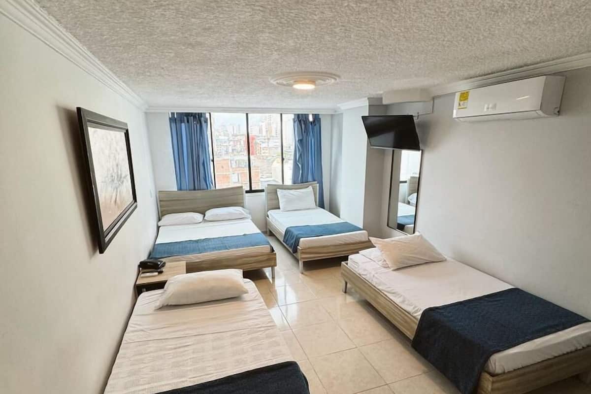 A hotel room with three single beds, a TV, an air conditioner, and a window with curtains.
