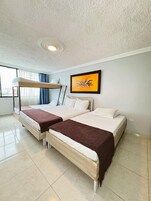 Una habitación con dos literas, un cuadro abstracto enmarco y una ventana con cortinas.