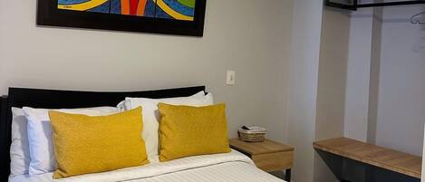 A hotel room with a bed, a nightstand, a TV, and a colorful abstract painting on the wall.