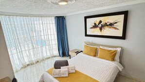 Ein Hotelzimmer mit Bett, Schreibtisch, Stuhl, Nachttisch und einem Fenster mit Vorhängen.