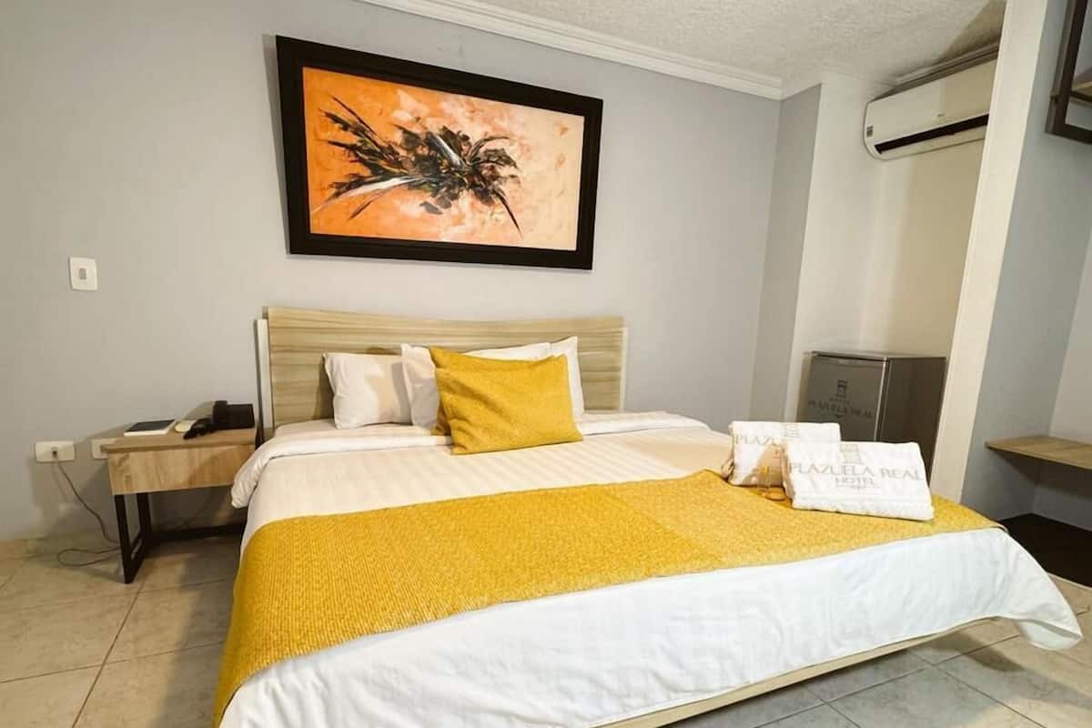 A neatly arranged hotel room with a large bed, a bedside table, a nightstand, and a wall-mounted air conditioning unit.