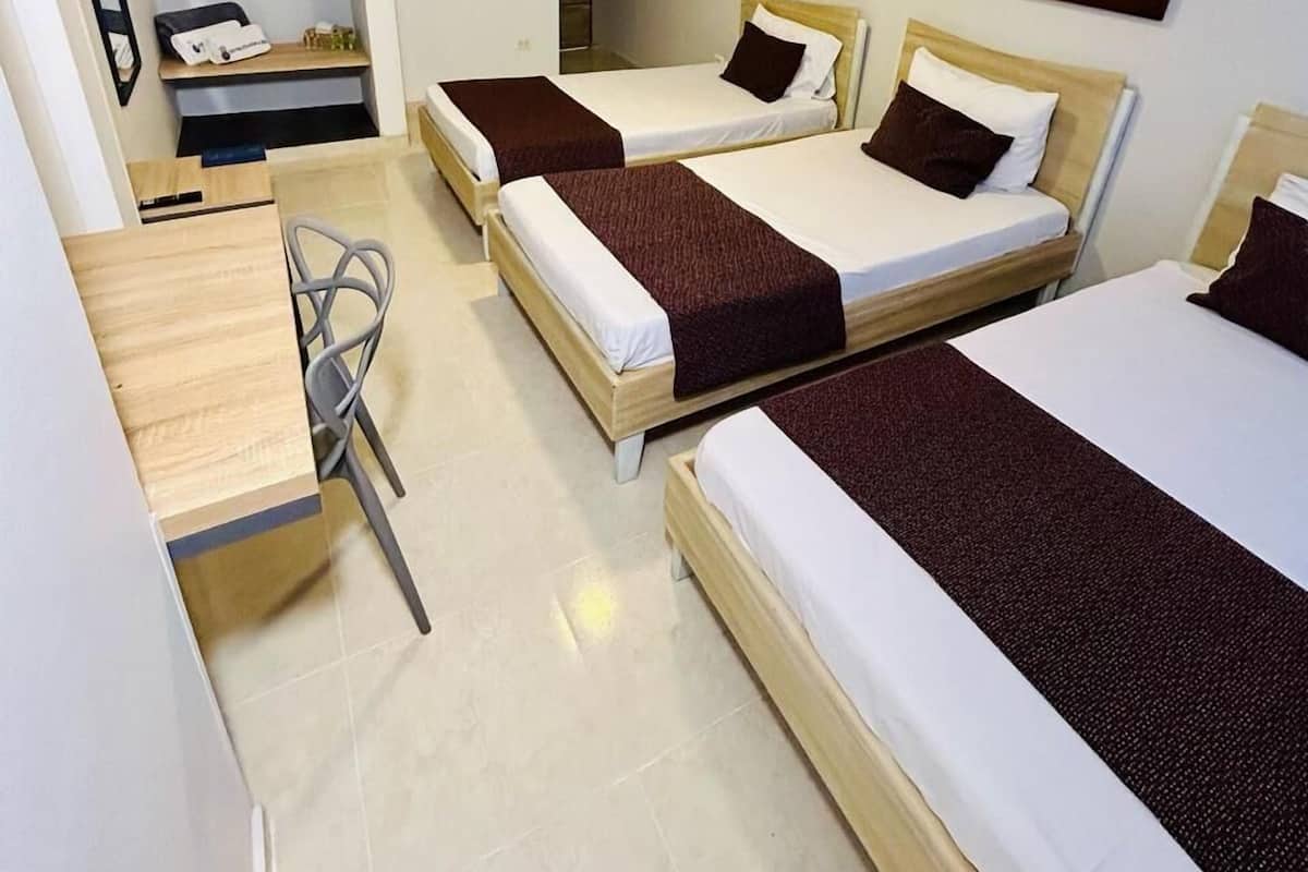 A hotel room with two single beds, a desk with a chair, a small table, and a ceiling light.