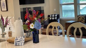 A dining area with a table set for two, a vase of flowers, a fireplace, and a television mounted on the wall.