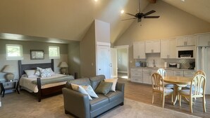 A spacious living area with a bed, sofa, and dining table, connected to a kitchen with white cabinets and appliances.