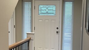 A staircase leading to a white door with a decorative glass panel, flanked by two windows with blinds.