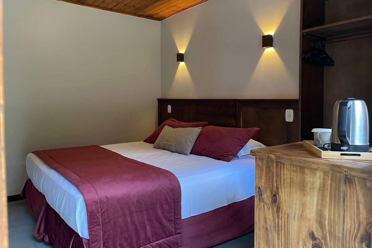A neatly made bed with a wooden headboard, two wall-mounted lights, and a wooden nightstand with a kettle.