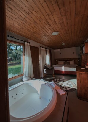 A wooden cabin interior with a large bathtub, a bed, and a view of the outdoors. - Hotel Cabanas Glamour (Gramado)