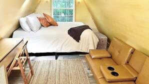 A cozy, triangular room with a bed, a small sofa, and a wooden table. - The EH Frame with Tree Pod in the woods! (Fountain Run)