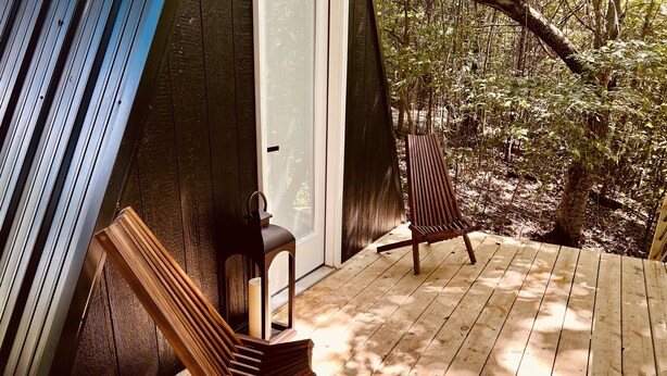 A wooden deck with two Adirondack chairs and a lantern, surrounded by trees. - The EH Frame with Tree Pod in the woods! (Fountain Run)